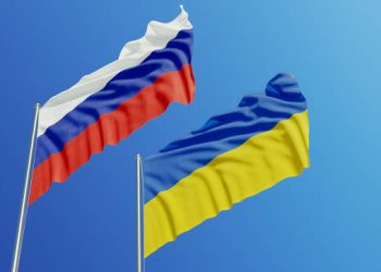 Russian and Ukrainian flags are waving with wind over  blue sky. Low angle view. Dispute and conflict concept. Horizontal composition with copy space.