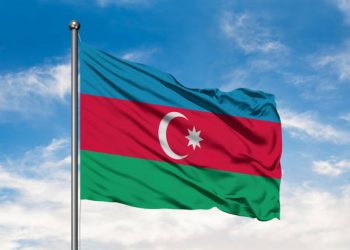 Flag of Azerbaijan waving in the wind against white cloudy blue sky. Azerbaijani flag.