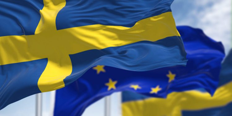 Detail of the national flag of Sweden waving in the wind with blurred european union flag in the background on a clear day. Democracy and politics. European country. Selective focus.