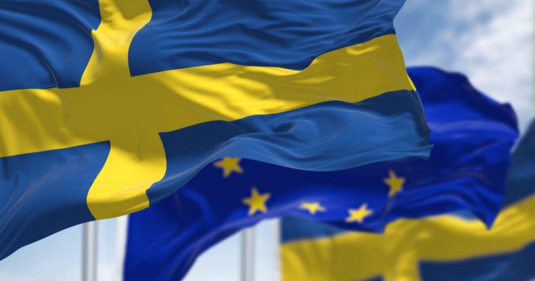 Detail of the national flag of Sweden waving in the wind with blurred european union flag in the background on a clear day. Democracy and politics. European country. Selective focus.