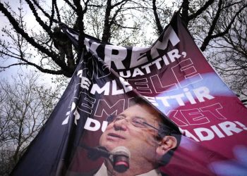 A man attaches a large banner of Istanbul's Mayor Ekrem Imamoglu in a tree in Istanbul, Turkey, Thursday, March 20, 2025, during a protest against the arrest of Imamoglu. (AP Photo/Emrah Gurel)