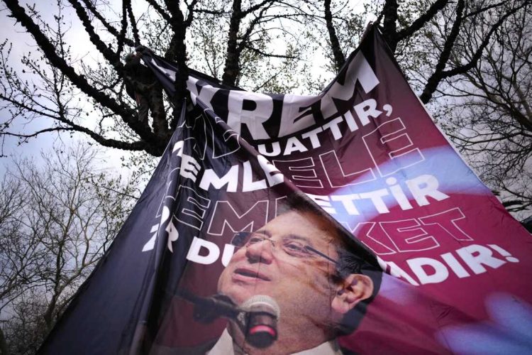 A man attaches a large banner of Istanbul's Mayor Ekrem Imamoglu in a tree in Istanbul, Turkey, Thursday, March 20, 2025, during a protest against the arrest of Imamoglu. (AP Photo/Emrah Gurel)