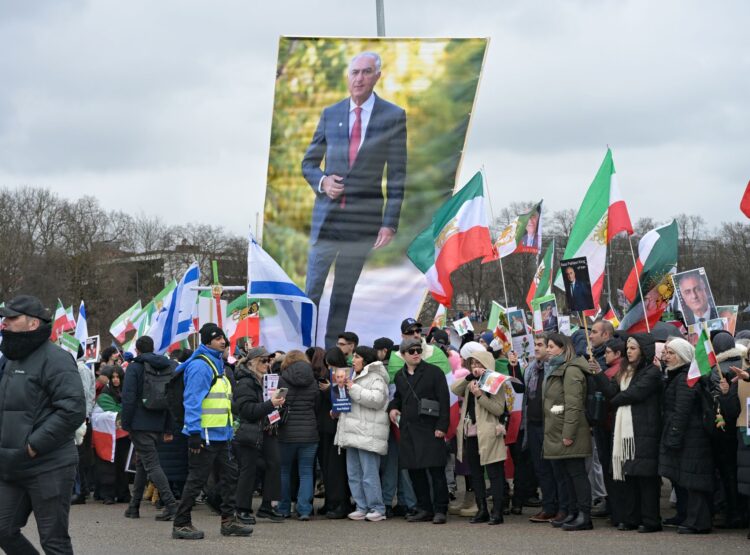 Teilnehmende einer Demonstration «Menschenrechte und Freiheit im Iran. Internationale Solidarität mit dem iranischen Volk» anlässlich der Münchner Sicherheitskonferenz stehen auf der Theresienwiese. Sie halten ein Überlebensgroßes Plakat von Reza Pahlavi hoch. Foto: Malin Wunderlich/dpa
